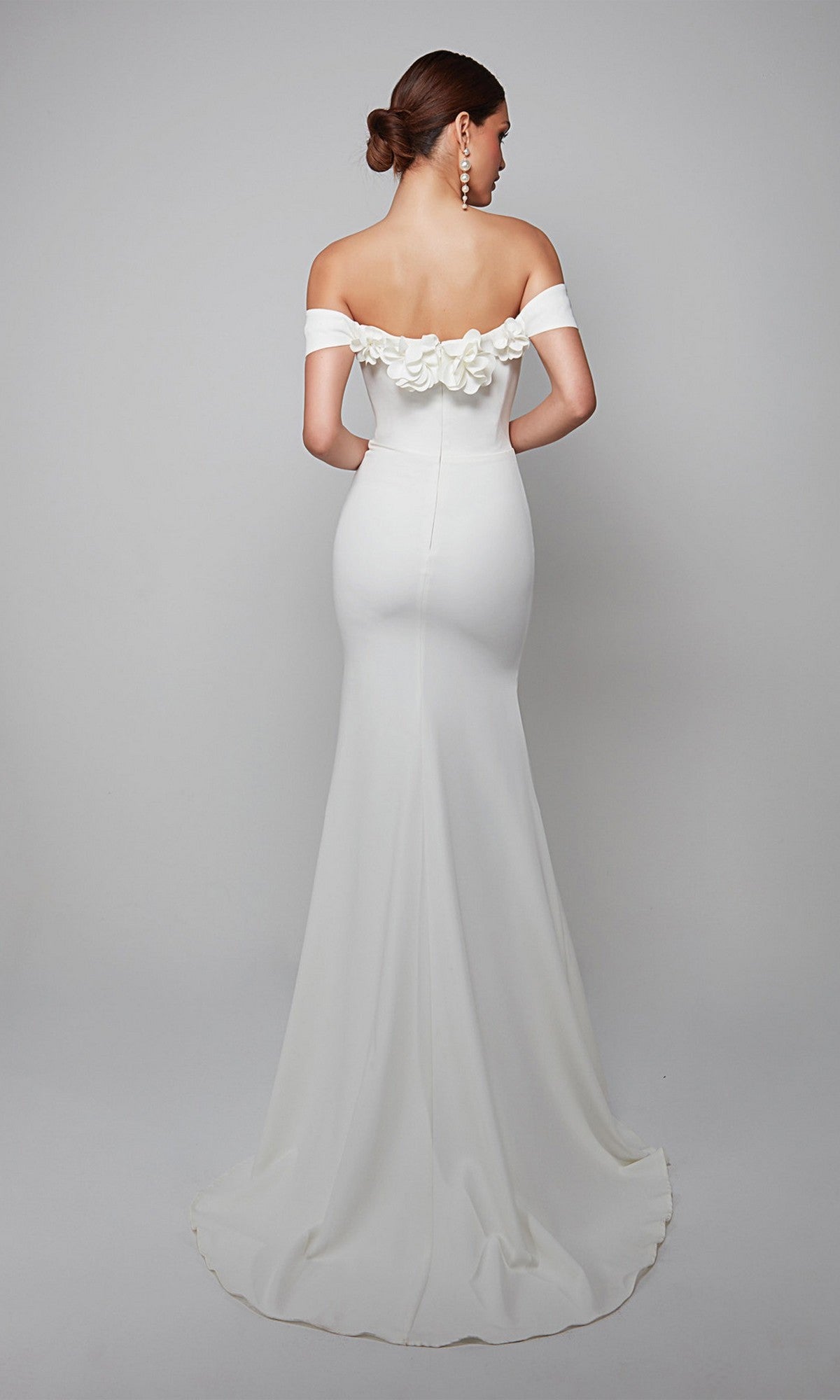 Woman in the Alyce 7062 long formal dress featuring an off-the-shoulder neckline, floor-length fitted silhouette, 3D floral back accents, and hair styled in a low bun.